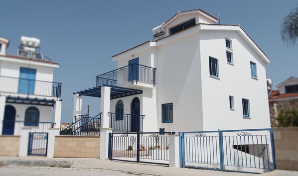 A two-story building with a white facade, blue shutters, and a balcony.
