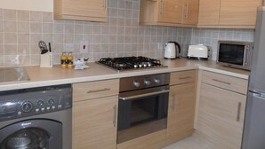 Eine kleine Küche mit Holzausstattung, einem Gasherd, einer Mikrowelle, einem Toaster und einem Geschirrspüler.