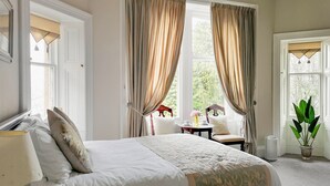 A bedroom with a large bed, a bedside table, a chair, and a window with curtains. - Heatherlie House Hotel (Selkirk)