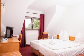 A hotel room with a bed, a desk, a chair, a TV, and a window with curtains. - Hotel Zehntscheune (Sinsheim)