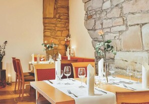 A restaurant with stone walls, wooden tables, and red cushioned chairs. - Hotel Zehntscheune (Sinsheim)