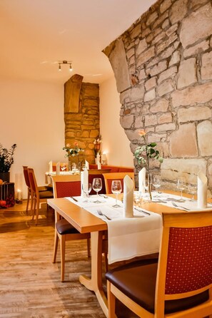 A dining area with wooden tables and chairs, stone walls, and candles. - Hotel Zehntscheune (Sinsheim)