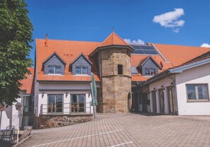 A building with a red-tiled roof, a stone tower, and a paved courtyard. - Hotel Zehntscheune (Sinsheim)