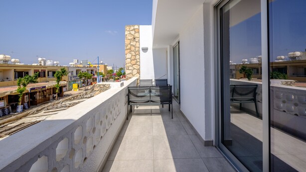 A balcony with a stone wall, a glass door, and a view of the cityscape. - Anonymous - 2BR - 2Floors - Central (Ayia Napa)