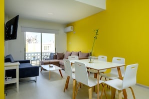 Ein modernes Wohnzimmer mit Essbereich, ausgestattet mit einer Couch, einem Fernseher und einem Tisch mit Stühlen.