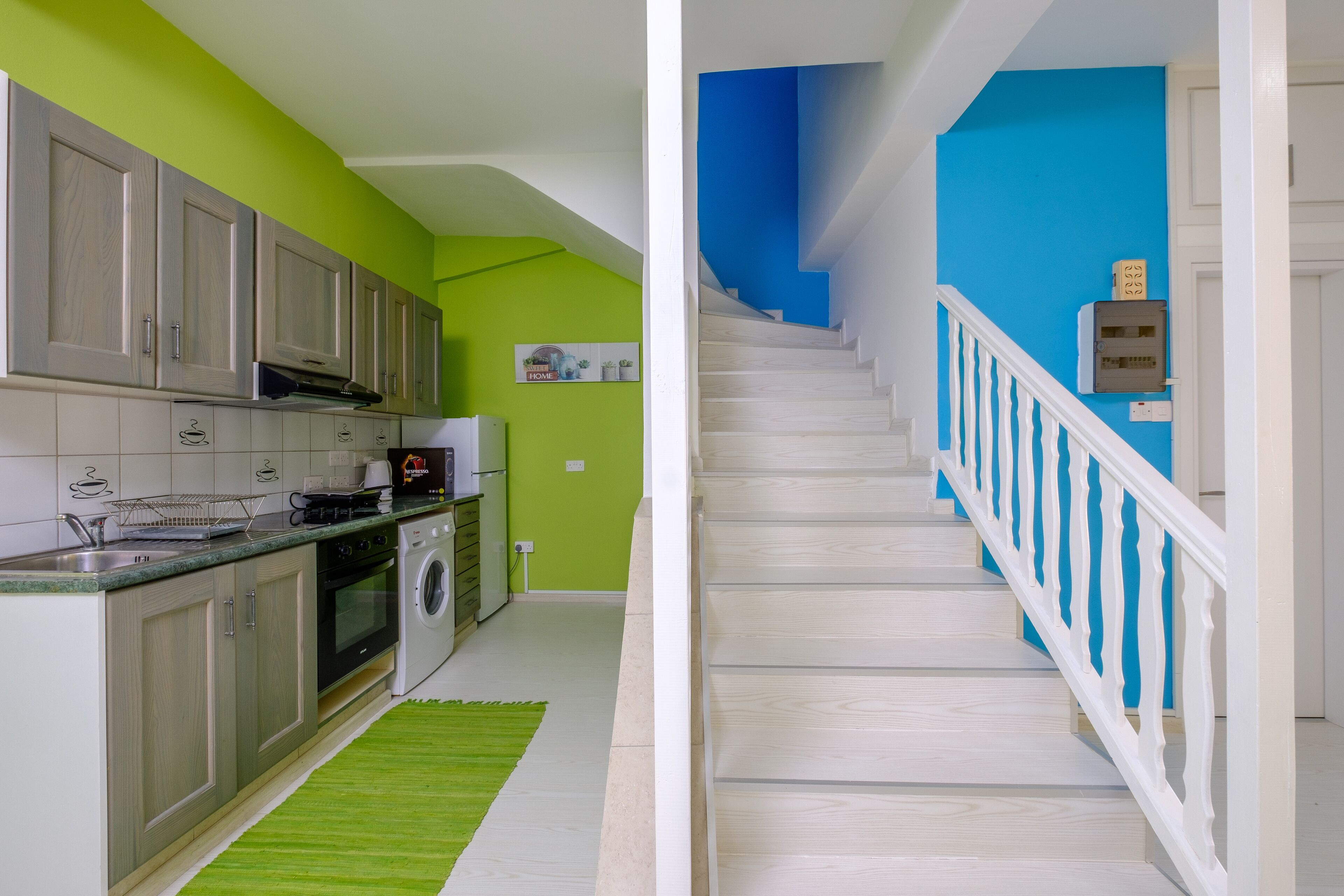 Una cocina moderna con electrodomésticos de acero inoxidable, una pared de acento verde y una escalera con barandillas blancas.