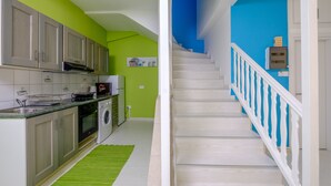 A modern kitchen with stainless steel appliances, a green accent wall, and a staircase with white railings. - Anonymous - 2BR - 2Floors - Central (Ayia Napa)