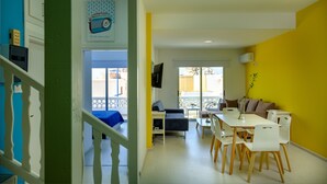 A bright room with a yellow wall, a white ceiling, and a blue door. There is a white table with chairs and a blue sofa. - Anonymous - 2BR - 2Floors - Central (Ayia Napa)