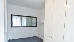 Een kleine kamer met een enkel bed, houten vloer, witte muren, een grote kast en een spiegel boven het bed.