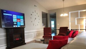 Ein Wohnzimmer mit Flachbildfernseher, Kamin, einer roten Couch mit Kissen und einer Wanduhr.