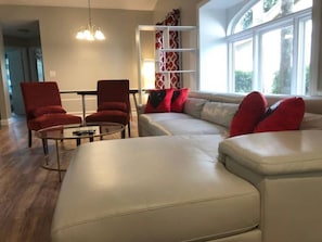 Ett modernt vardagsrum med en beige soffa, röda fåtöljer, ett soffbord i glas och en vit hyllsektion.