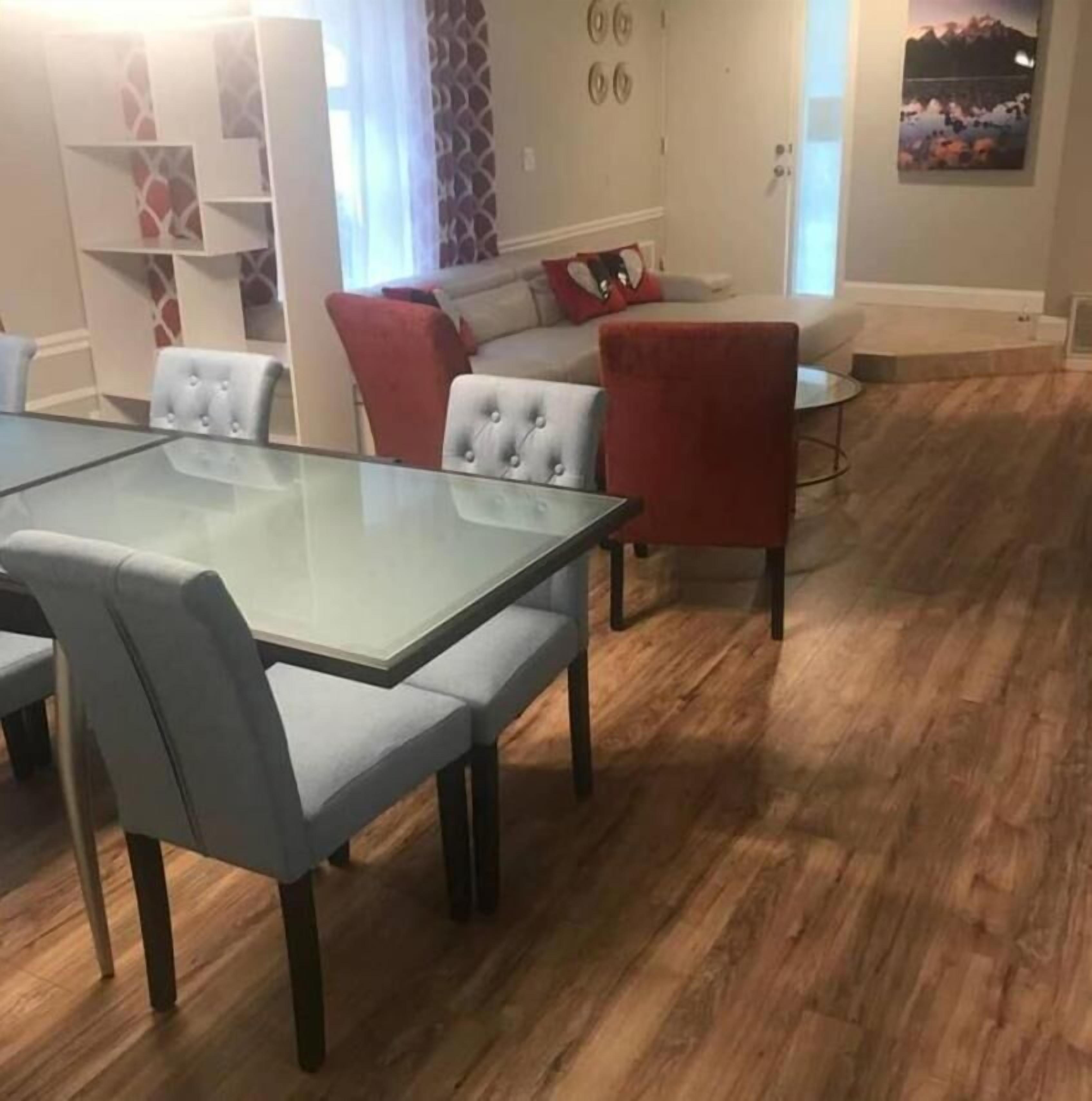 A dining area with a glass-top table, grey upholstered chairs, and a red chair.