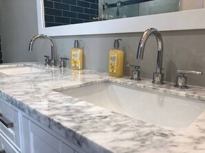 A bathroom with a double sink, two faucets, and two bottles of soap on the countertop.