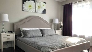 Une chambre à coucher avec un grand lit, deux tables de chevet et une fenêtre avec des rideaux.