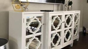 Un meuble blanc orné de motifs complexes découpés, un téléviseur à écran plat fixé au-dessus, et un petit objet décoratif posé sur le meuble.
