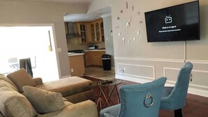 A living room with a beige sofa, a blue armchair, a flat-screen TV displaying a signal strength message, and a kitchen in the background. - 6151 Sandcrest · Next to Universal. Pool Sleep 9. Walk to Park (Orlando)