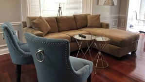 A living room with a large L-shaped sectional sofa, two matching armchairs, a small round coffee table, and a tripod floor lamp. - 6151 Sandcrest · Next to Universal. Pool Sleep 9. Walk to Park (Orlando)