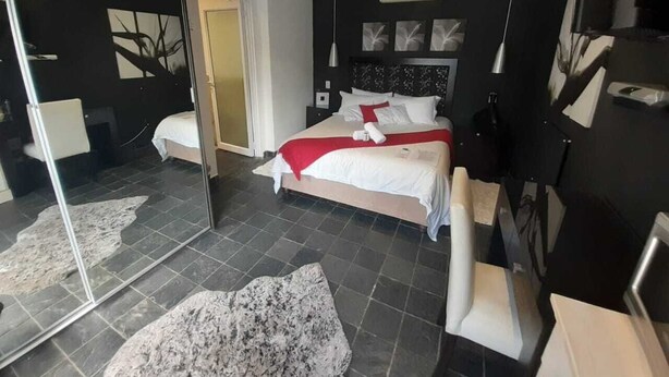 Un dormitorio moderno con cama, espejo, cómoda y un amplio ventanal.