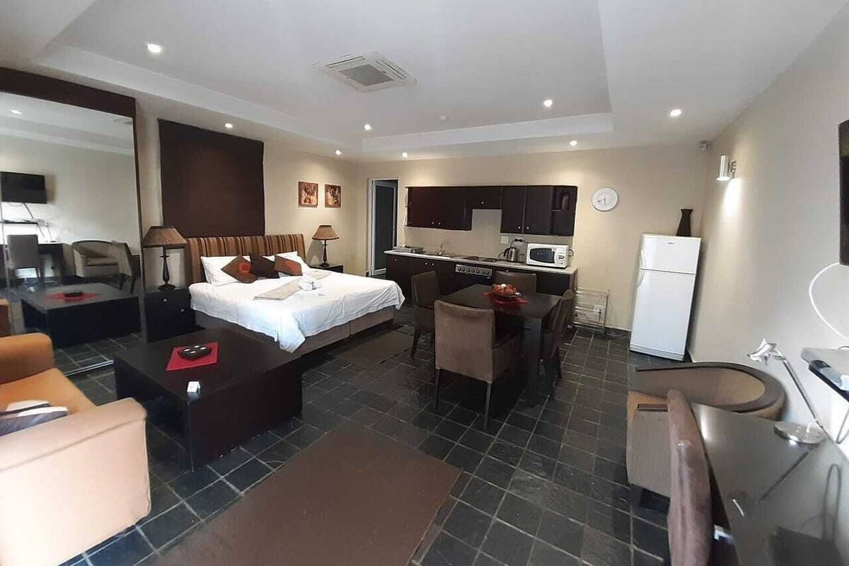 Una habitación de hotel con cama, escritorio, silla, kitchenette pequeño y baño.