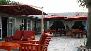 Un patio al aire libre con mobiliario de madera, sombrillas rojas y piso de baldosas.