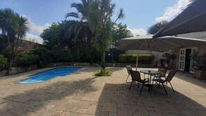 Un patio trasero con piscina, mobiliario de jardín y una zona de estar cubierta.