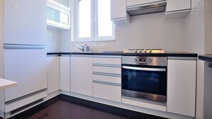 Een moderne keuken met witte kastjes, een inbouwoven en een raam boven de spoelbak.
