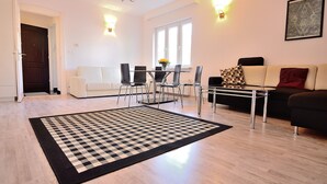 Een moderne woonkamer met een eetgedeelte, met een geruit tapijt, een bank, een salontafel en een eettafel met stoelen.