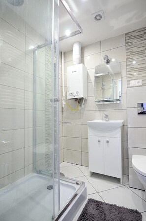 A modern bathroom with a glass shower enclosure, a white sink, and a mirror above the sink. - Victus Apartamenty - La Figure (Sopot)