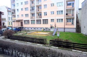 A multi-story residential building with balconies, a small playground, and a parking area with cars. - Victus Apartamenty - La Figure (Sopot)