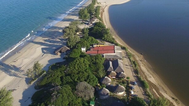 An aerial view of a beachside property with a sandy beach, a few thatched-roof huts, and a large body of water. - Macaneta Holiday Resort (Marracuene)