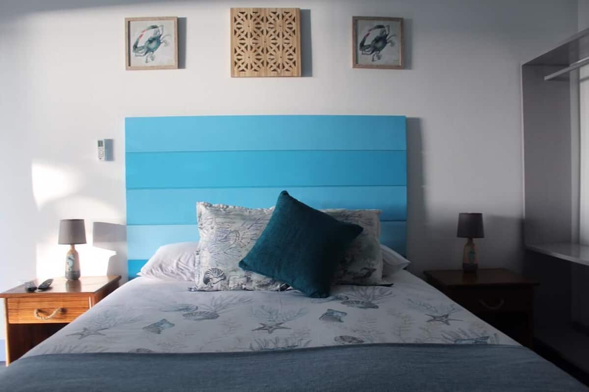A bedroom with a blue headboard, a bed with floral bedding, two bedside lamps, and artwork on the walls.