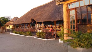 A thatched-roof building with outdoor seating areas and a large window on the right side. - Macaneta Holiday Resort (Marracuene)