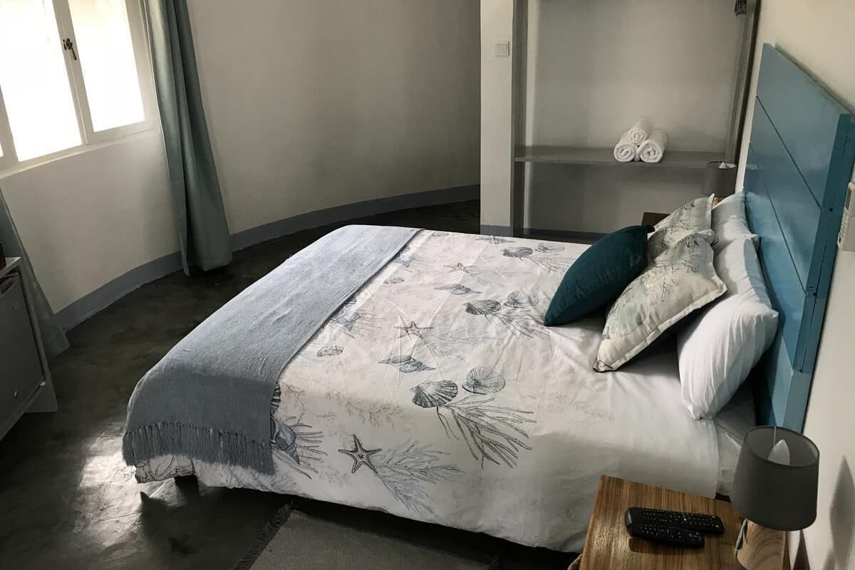 A bedroom with a bed, a nightstand, a bedside table, a wardrobe, and a window with curtains.