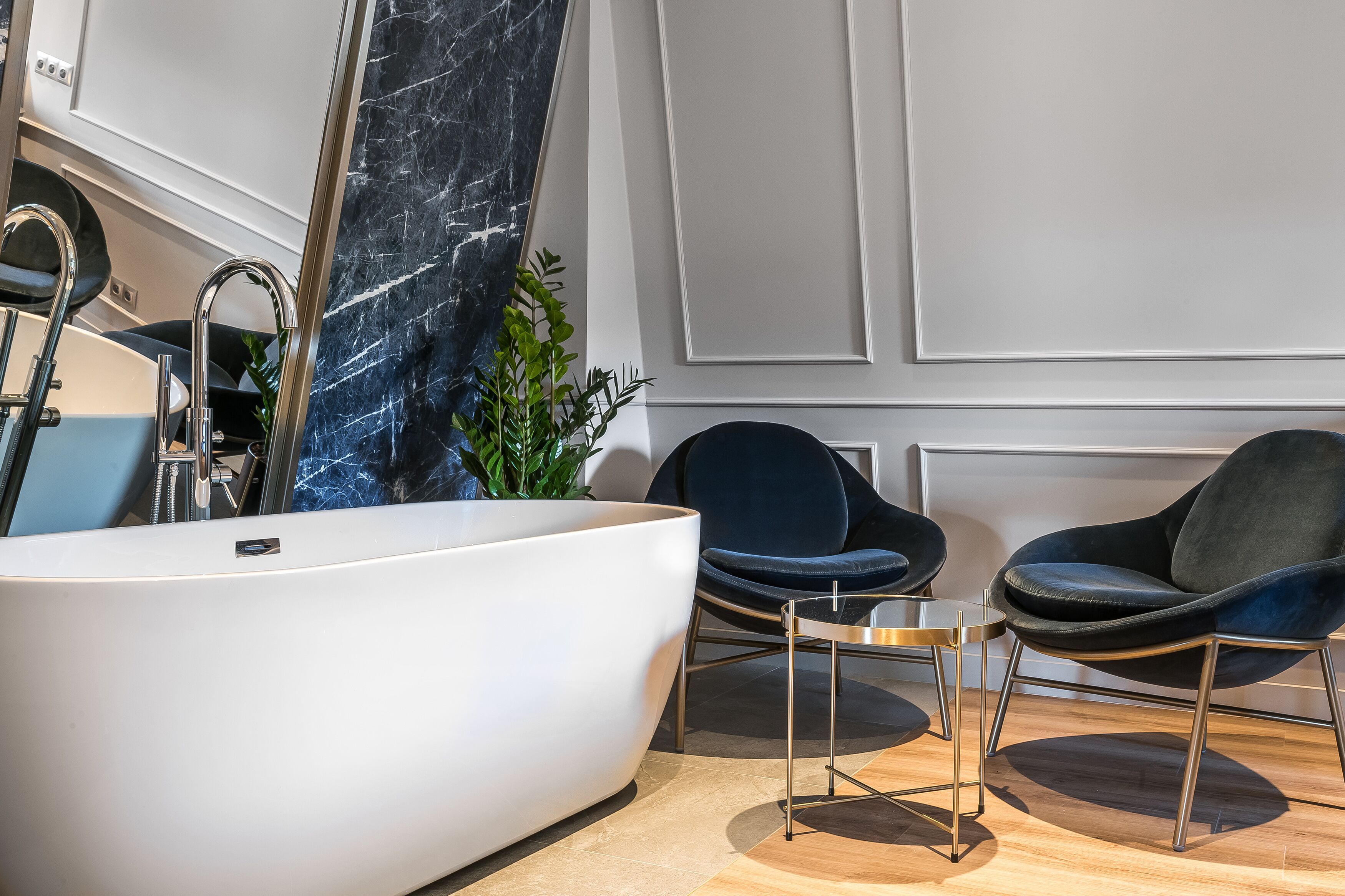 Une salle de bain moderne avec une grande baignoire blanche, deux chaises bleu foncé, une petite table et une plante en pot.