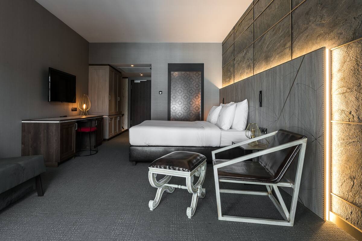 Ett modernt hotellrum med en säng, ett skrivbord, en stol och en TV.