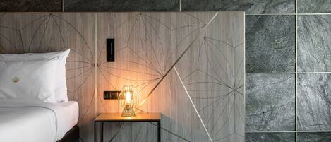 Una habitación de hotel moderna con una cama, una mesita de noche con lámpara y un diseño geométrico en la pared.