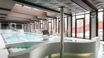 Una piscina interior con suelo y paredes de azulejos, rodeada de zonas de estar y grandes ventanales.