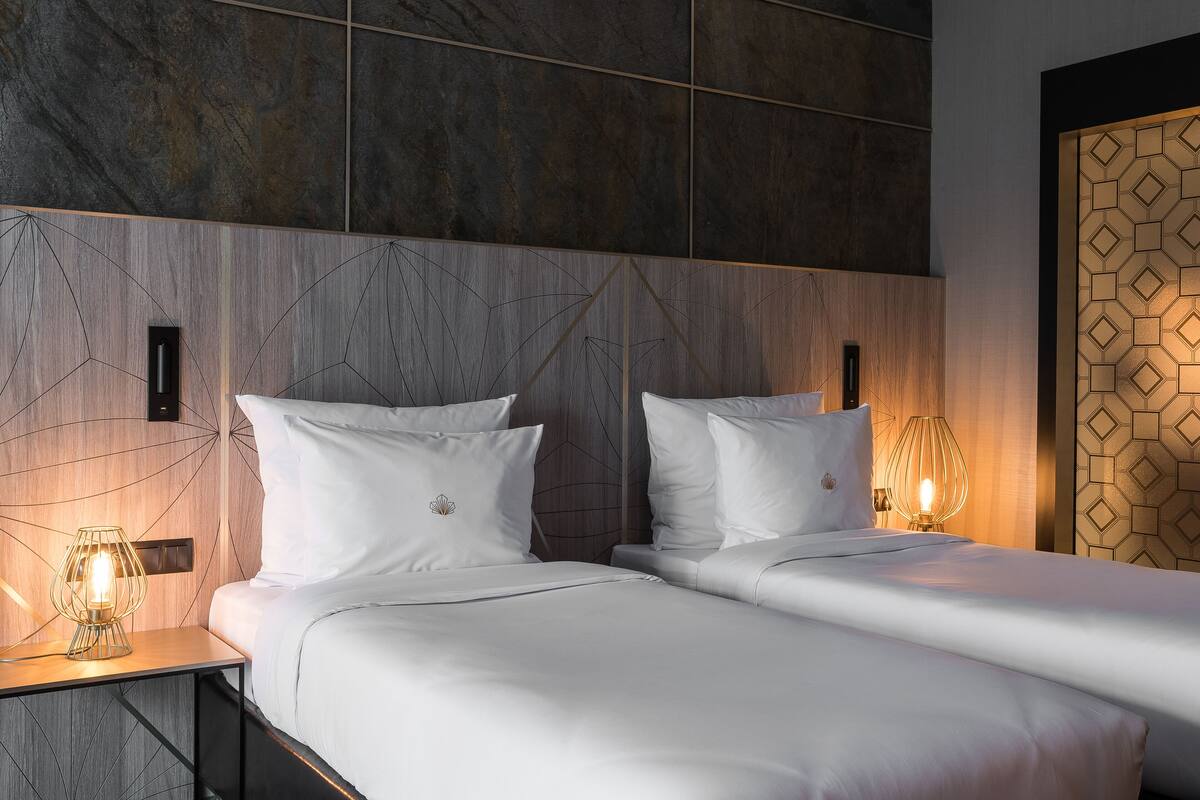Ett hotellrum med två sängar, en sänggavel i trä, ett geometriskt mönster på väggen och en dörr med ett dekorativt mönster.