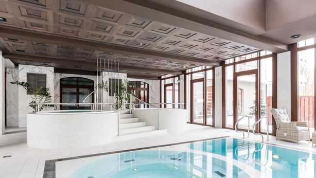 Una piscina interior con paredes de vidrio transparente, suelo de baldosas y un diseño moderno en el techo.