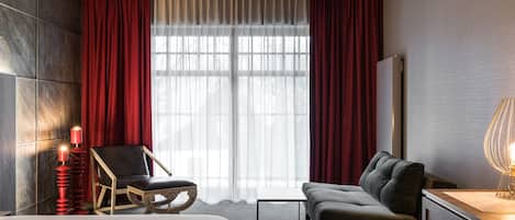A hotel room with a bed, a sofa, a chair, a small table, and a lamp.