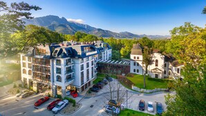 Un hotel de varios pisos con un diseño arquitectónico moderno, que presenta una combinación de balcones y ventanas amplias, ubicado en una zona verde y exuberante con montañas al fondo.