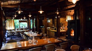 A rustic restaurant interior with wooden tables, wicker chairs, hanging pendant lights, a brick wall, and a fireplace. - Młyn Klekotki spa resort (Gmina Godkowo)