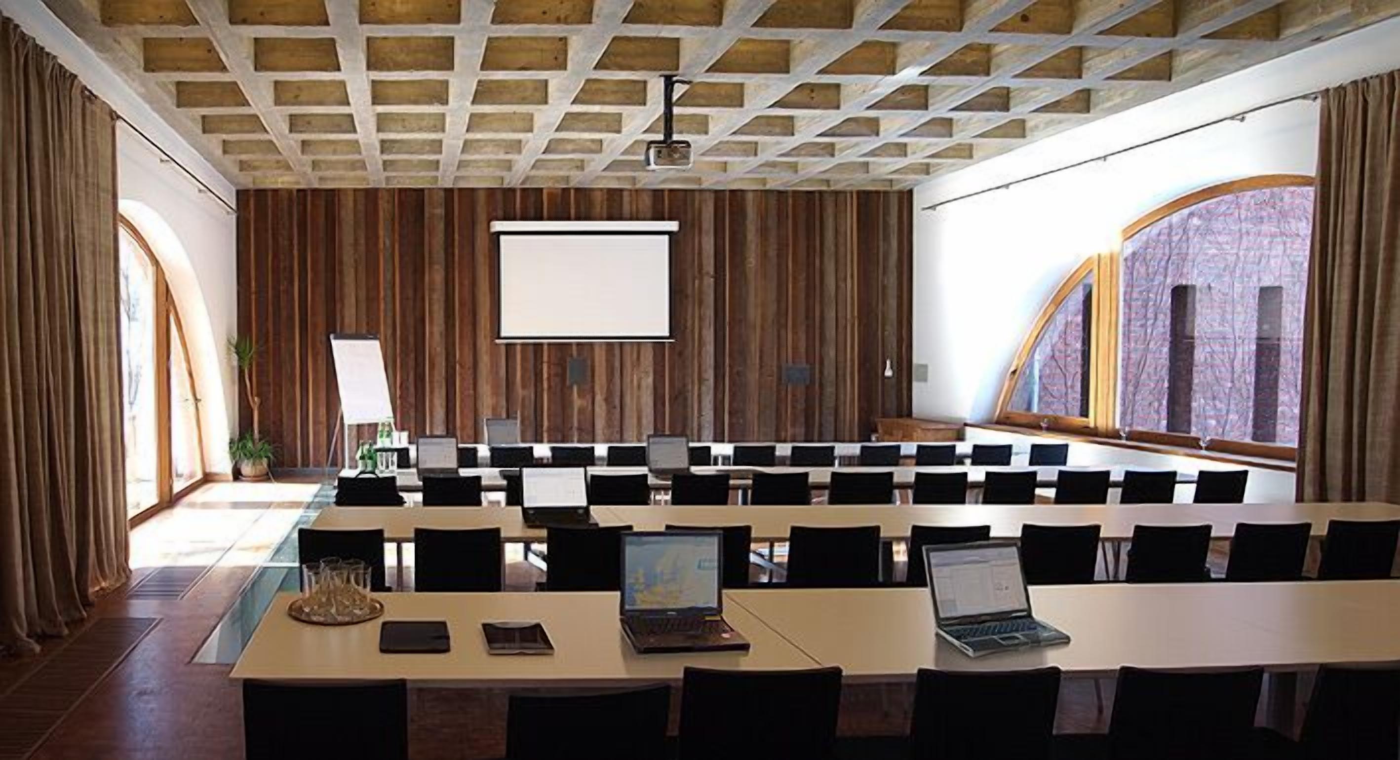 A conference room with a long table, multiple chairs, a projector screen, and a large window with curtains.
