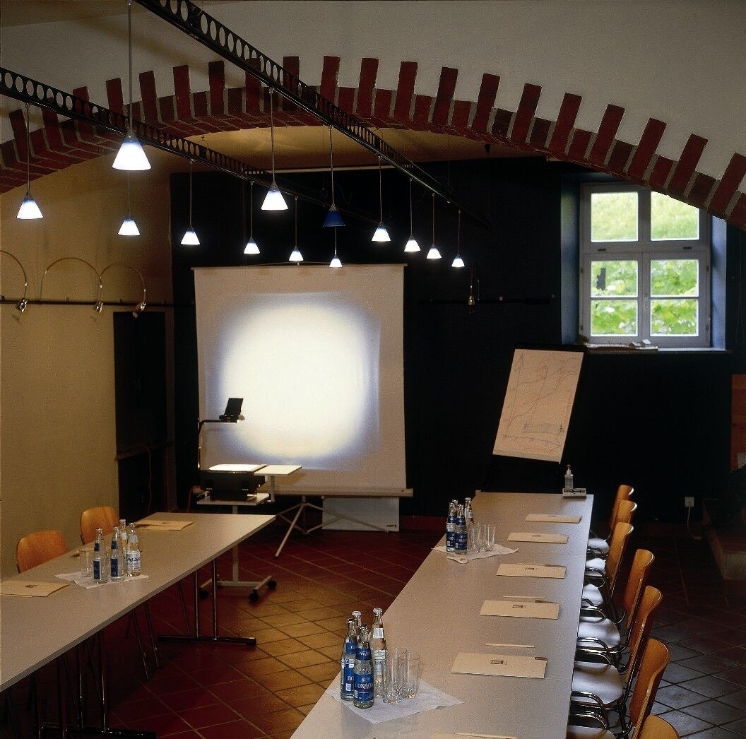 Una sala conferenze con un lungo tavolo, sedie, uno schermo per proiettore e una finestra.