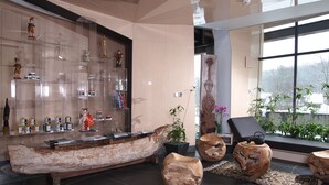 A modern interior with a large wooden boat centerpiece, clear glass shelving with various items, and a large window with a view of snow-covered trees. - Młyn Klekotki spa resort (Gmina Godkowo)