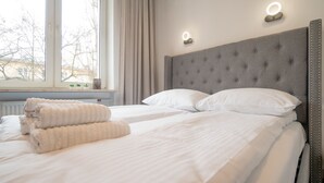 A hotel room with a large window, a grey upholstered headboard, white bedding, and two bedside lamps. - Frey Homes City Centre Plac Zbawiciela (Warsaw)