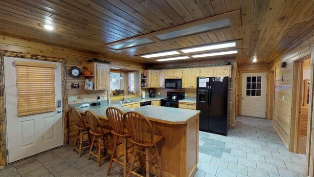 A wooden cabin-style kitchen with a central island, wooden cabinets, and a black refrigerator.