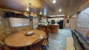 A wooden interior with a dining table, chairs, a sofa, and a kitchen area.