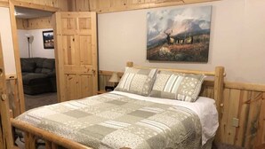 A wooden-framed bed with a quilted bedspread in a room with wooden walls and a painting of a deer on the wall.