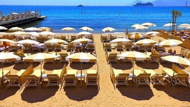 A beach with rows of sun loungers and umbrellas, a pier extending into the water, and a cruise ship in the distance. - Charming 5 bedroom, 3 bathroom Villa in gated domain near Valbonne with sea view (Opio)